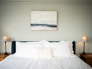 A bed with white pillows and a small decorative pillow between two bedside tables with lamps hanging a landscape painting above the bed at Haulfryn in Barmouth