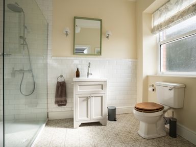 A bathroom with a shower, sink with cabinet and mirror, toilet with wooden seat and patterned floor tiles at Haulfryn in Barmouth