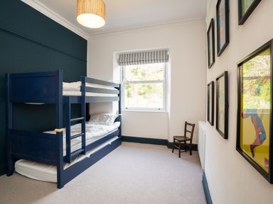A bedroom with a blue bunk bed a window a wooden chair and framed pictures on the wall at Haulfryn in Barmouth
