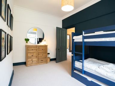 A bedroom with a blue bunk bed wooden dresser round mirror and framed pictures on the wall at Haulfryn in Barmouth