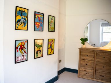 A wall with six framed superhero posters next to a wooden dresser with a round mirror and a small plant at Haulfryn in Barmouth