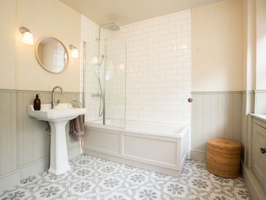 A bathroom with a pedestal sink a bathtub with shower a round mirror and patterned floor tiles at Haulfryn in Barmouth