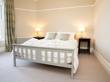 A bedroom with a grey wooden bed a white duvet patterned pillows two bedside tables with lamps and patterned curtains at Haulfryn in Barmouth