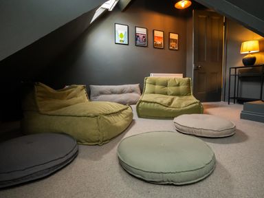 A room with floor cushions and bean bag chairs under a slanted ceiling with framed pictures on the wall at Haulfryn in Barmouth