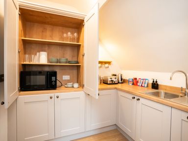 A kitchen corner with white cabinets open shelving microwave toaster kettle snacks and a stainless steel sink at Haulfryn in Barmouth