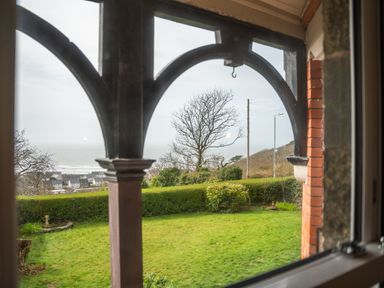 A view of a garden with bushes and trees with houses and the sea in the background seen through window arches