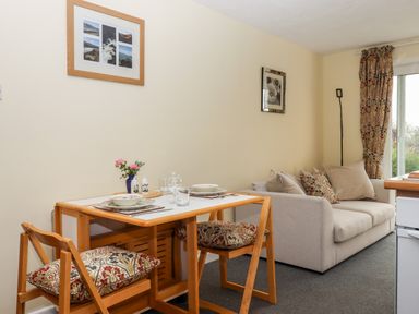 A dining table with two chairs and plates next to a sofa with cushions and a floor lamp at Mabel's View in East Allington Devon