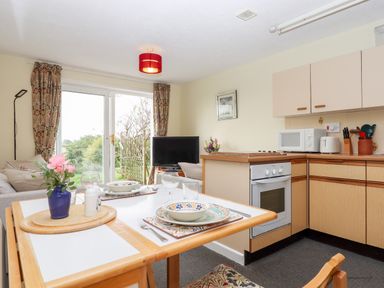 A kitchen and dining area with table set for two and a living room with television and sofa at Mabel's View in East Allington Devon