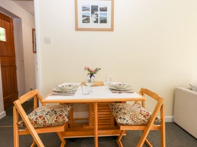 A dining table with two wooden chairs with cushions and table settings in a room at Mabel's View in East Allington Devon