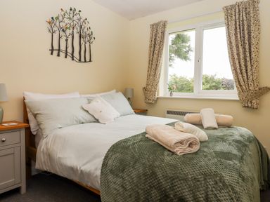 A bedroom with a bed covered with pillows and folded towels near a window with curtains at Mabel's View in East Allington Devon