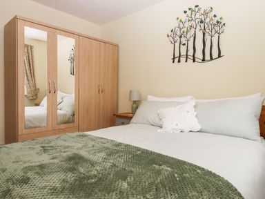 A bedroom with a bed a green blanket a wooden wardrobe with mirrors and a tree wall decoration at Mabel's View in East Allington Devon