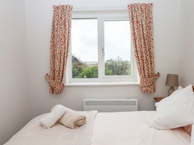 A bedroom with a bed with folded towels on it a window with patterned curtains and a nightstand with a lamp at Mabel's View in East Allington Devon