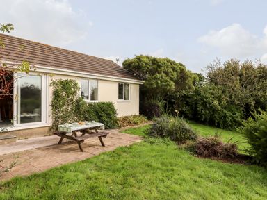 A house with a wooden picnic table on a stone patio and bushes and grass in the garden at Mabels View in East Allington Devon