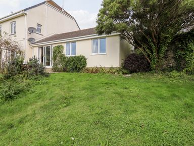 A garden with grass and bushes behind a cream-colored house at Mabel's View in East Allington Devon