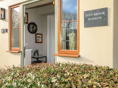 An open window and door with a view into a room with a small table and plant a sign on the wall saying Inny Brook Burrow at Inny Brook Burrow in Davidstow near Camelford