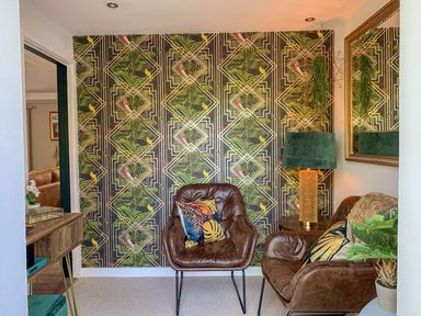 A small sitting area with two brown leather chairs, a green lampshade on a side table, a large mirror, patterned wallpaper, and indoor plants at Inny Brook Burrow in Davidstow near Camelford