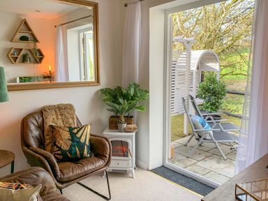 A living room with leather chairs and a small stove next to a glass door overlooking a patio with two chairs at Inny Brook Burrow Davidstow near Camelford