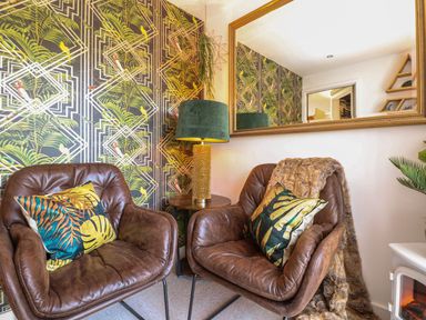 A seating area with two brown leather chairs with patterned cushions a round side table with a lamp and a large mirror on the wall at Inny Brook Burrow in Davidstow near Camelford