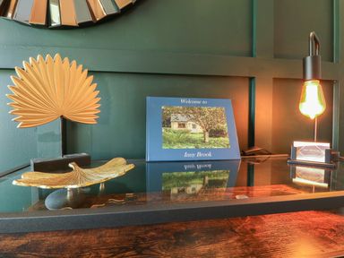 A glass desk with a blue welcome book a golden leaf dish a golden palm decoration and a lamp at Inny Brook Burrow in Davidstow near Camelford