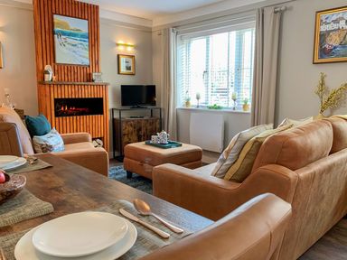 A living room with tan sofas a wooden coffee table a fireplace and a window with blinds at Inny Brook Burrow in Davidstow near Camelford