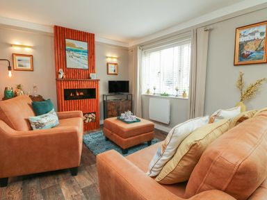 A living room with orange sofas a wooden floor a red brick fireplace and paintings on the walls at Inny Brook Burrow Davidstow near Camelford