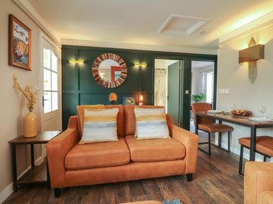 A living room with a brown sofa and cushions a wooden side table with a vase and a dining table with chairs at Inny Brook Burrow in Davidstow near Camelford