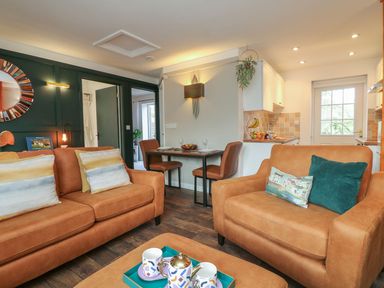A living room with brown sofas and pillows a small dining table with two chairs and a kitchen visible at Inny Brook Burrow in Davidstow near Camelford