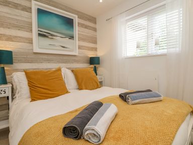 A bedroom with a bed with mustard yellow bedding pillows and rolled towels beside a window with blinds and lamps at Inny Brook Burrow in Davidstow near Camelford