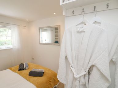 A bedroom with two white robes hanging on hooks yellow blanket on bed and folded towels on it at Inny Brook Burrow in Davidstow near Camelford