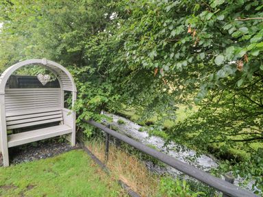 A wooden bench near a small stream with trees and a fence in a garden at Inny Brook Burrow Davidstow near Camelford