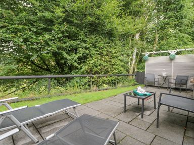 A patio area with lounge chairs a table and two chairs near trees and a wooden fence at Inny Brook Burrow in Davidstow near Camelford