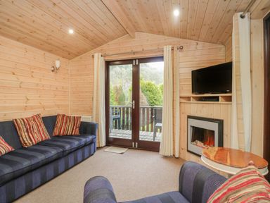 A living room with blue striped sofas red striped cushions a wooden round table a wall mounted tv an electric fireplace and glass doors leading outside at Canadian Cabin No 39 in Keswick