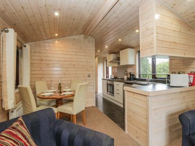 A kitchen and dining area with wooden walls and ceiling and a small round dining table with four chairs at Canadian Cabin No 39 in Keswick