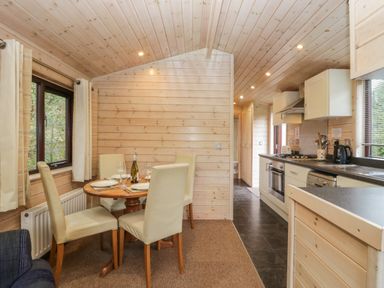 A dining area with a round wooden table and four chairs next to a kitchen with cabinets and appliances at Canadian Cabin No 39 in Keswick