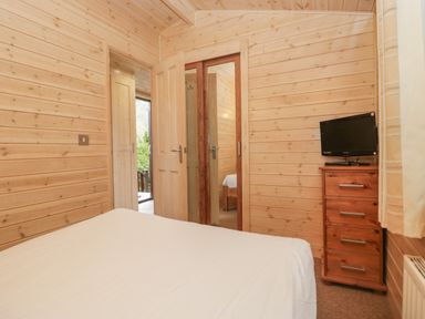 A bedroom with a bed a wooden drawer with a TV and a door with a mirror inside Canadian Cabin No 39 in Keswick