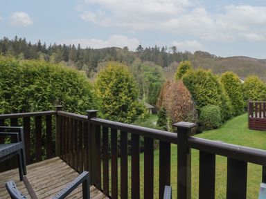 A wooden balcony with chairs overlooking a garden with bushes and trees at Canadian Cabin No 39 in Keswick