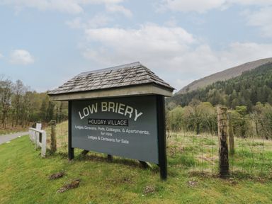 A sign for Low Briery Holiday Village near a road with trees and hills in the background at Dogwood Timber Lodge in Keswick