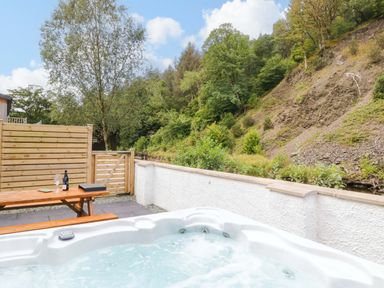 A hot tub and table with drinks in an outdoor area at Riverside Cottage No 4 Keswick