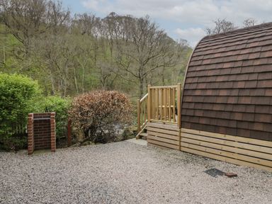A gravel area next to a wooden pod with steps and railing surrounded by trees at Pod No 6 Keswick