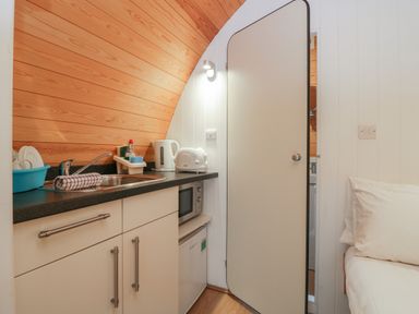 A kitchenette with a sink, kettle, toaster, microwave, mini fridge, and a partially open door next to a bed at Pod No 6 in Keswick