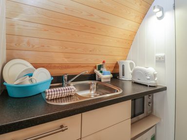 A small kitchenette with a sink, a blue dish rack holding dishes, a kettle, a toaster, and a microwave at Pod No 6 in Keswick