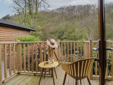 A wooden balcony with a chair a small table holding a bottle and two glasses and a hat hanging on the railing at Pod No 28 in Keswick