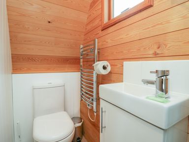 A bathroom with a toilet a small sink a towel rail with toilet paper and wooden panel walls at Pod No 28 in Keswick