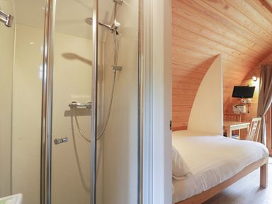 A bedroom with a bed table chairs TV and a view of a shower cubicle at Pod No 28 in Keswick