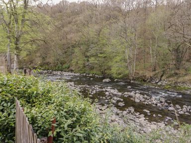 A river with rocks and trees along the bank with a wooden fence and green bushes at Pod No 28 in Keswick