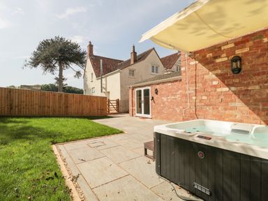 An outdoor patio with a hot tub grass lawn and a brick building at The Nest in North Petherton