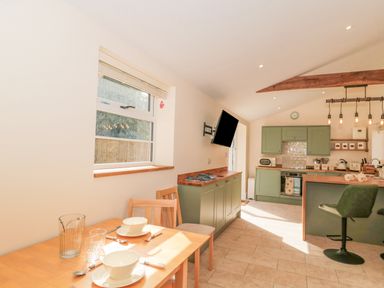 A kitchen with green cabinets a wooden dining table set with bowls and glasses and a mounted television at The Nest in North Petherton