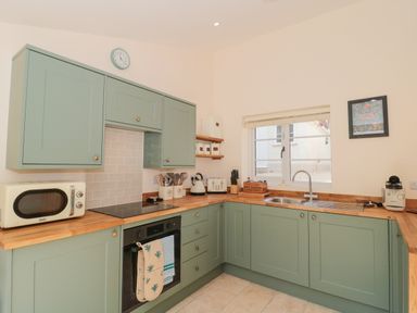 A kitchen with green cabinets wooden countertops a microwave oven and a window at The Nest in North Petherton