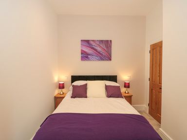 A bedroom with a double bed purple and white bedding two bedside tables with lamps and a wooden door at The Nest in North Petherton