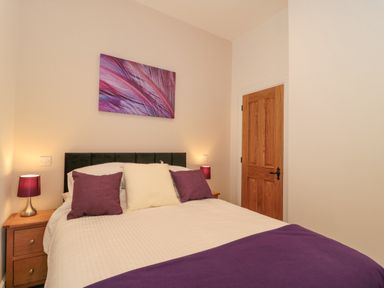 A bedroom with a double bed purple cushions and lamps and a wooden door at The Nest in North Petherton